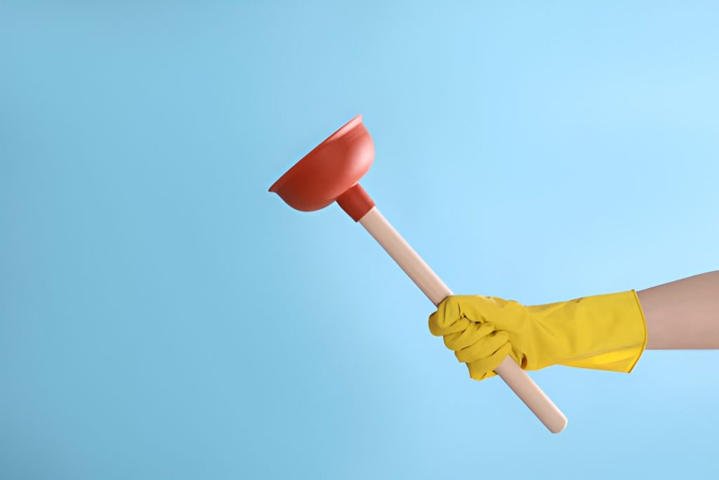 close-up of a hand in a yellow glove, holding an orange plunger
